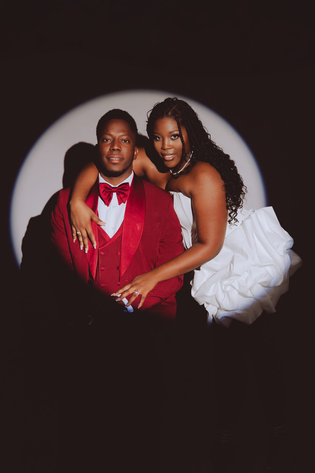 Couple de fiancés en costume rouge et robe blanche sous un cercle de lumière