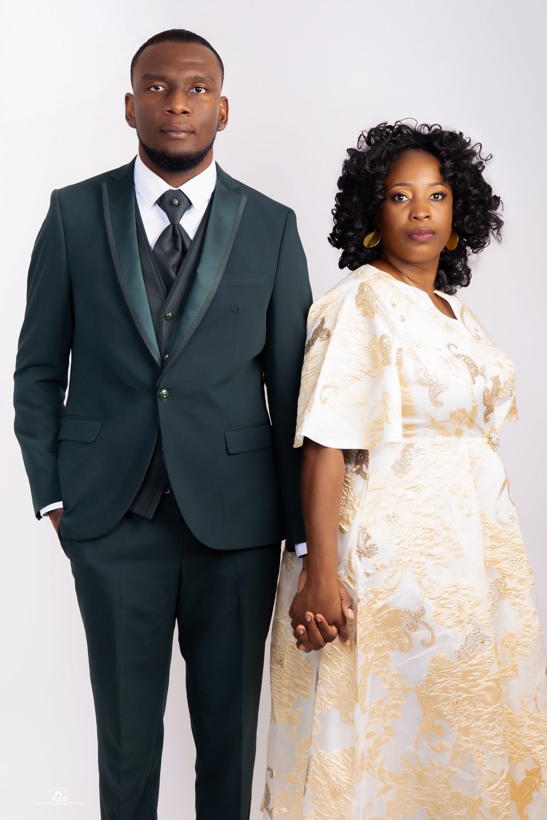 Couple main dans la main en studio, costume vert et robe brodée or